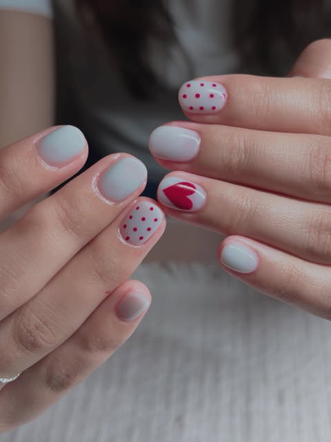 Milky white nails with red heart and polka accents.