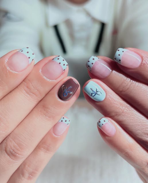 Short blue polka-dot French tips with silver bow charms by Lina.